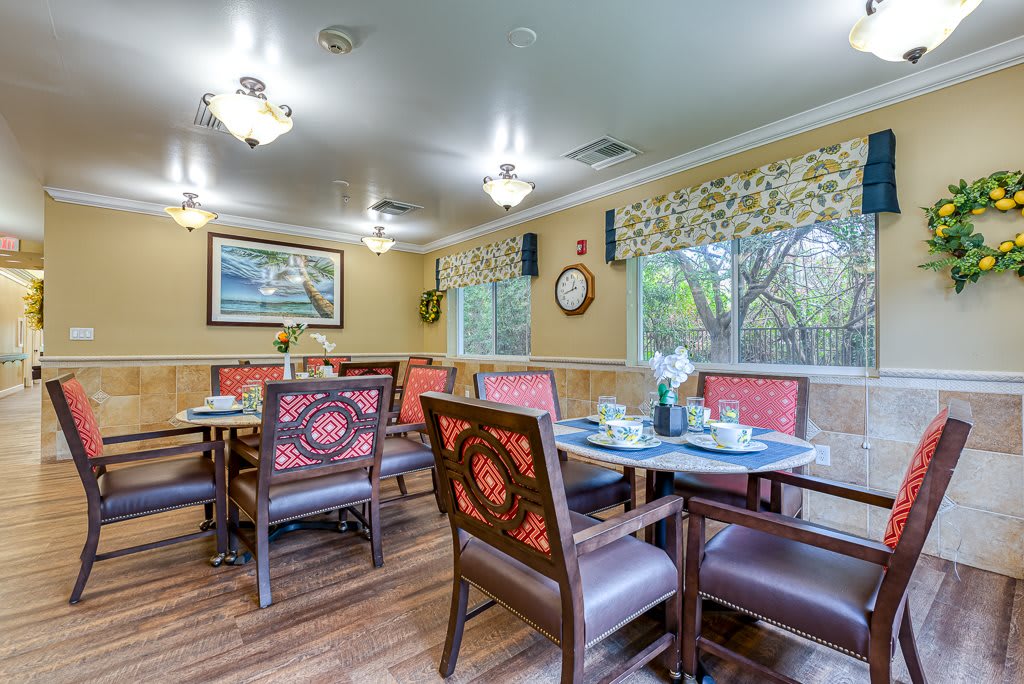 A cozy dining room with neatly arranged tables and chairs, featuring large windows and elegant decor.