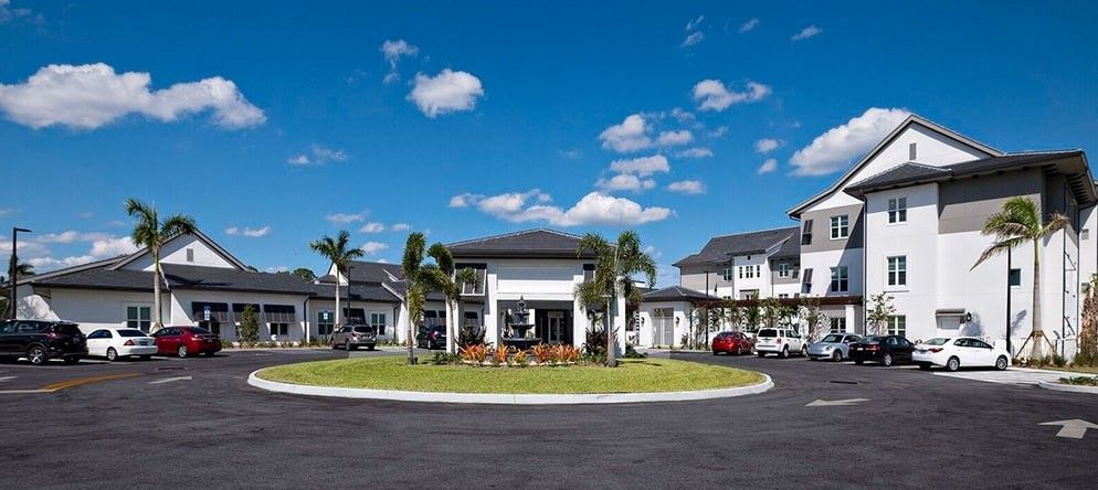 A modern residential building with palm trees and a circular driveway.