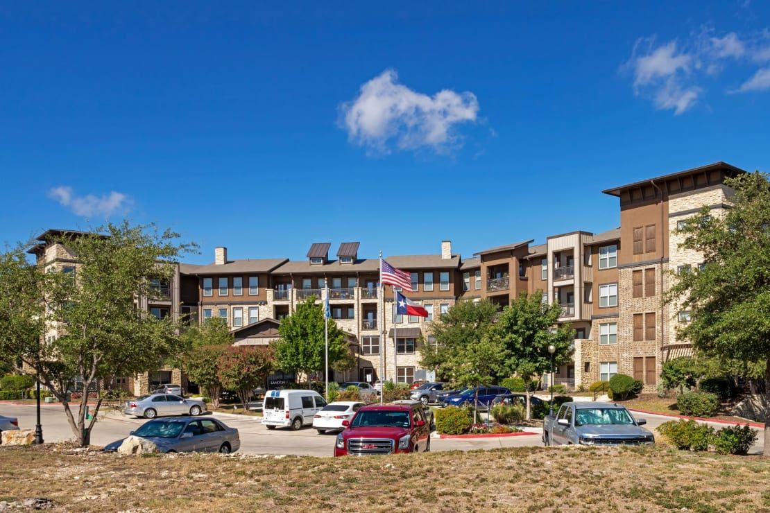 A multi-story building with a parking lot and cars in front, under a clear blue sky with a few clouds.
