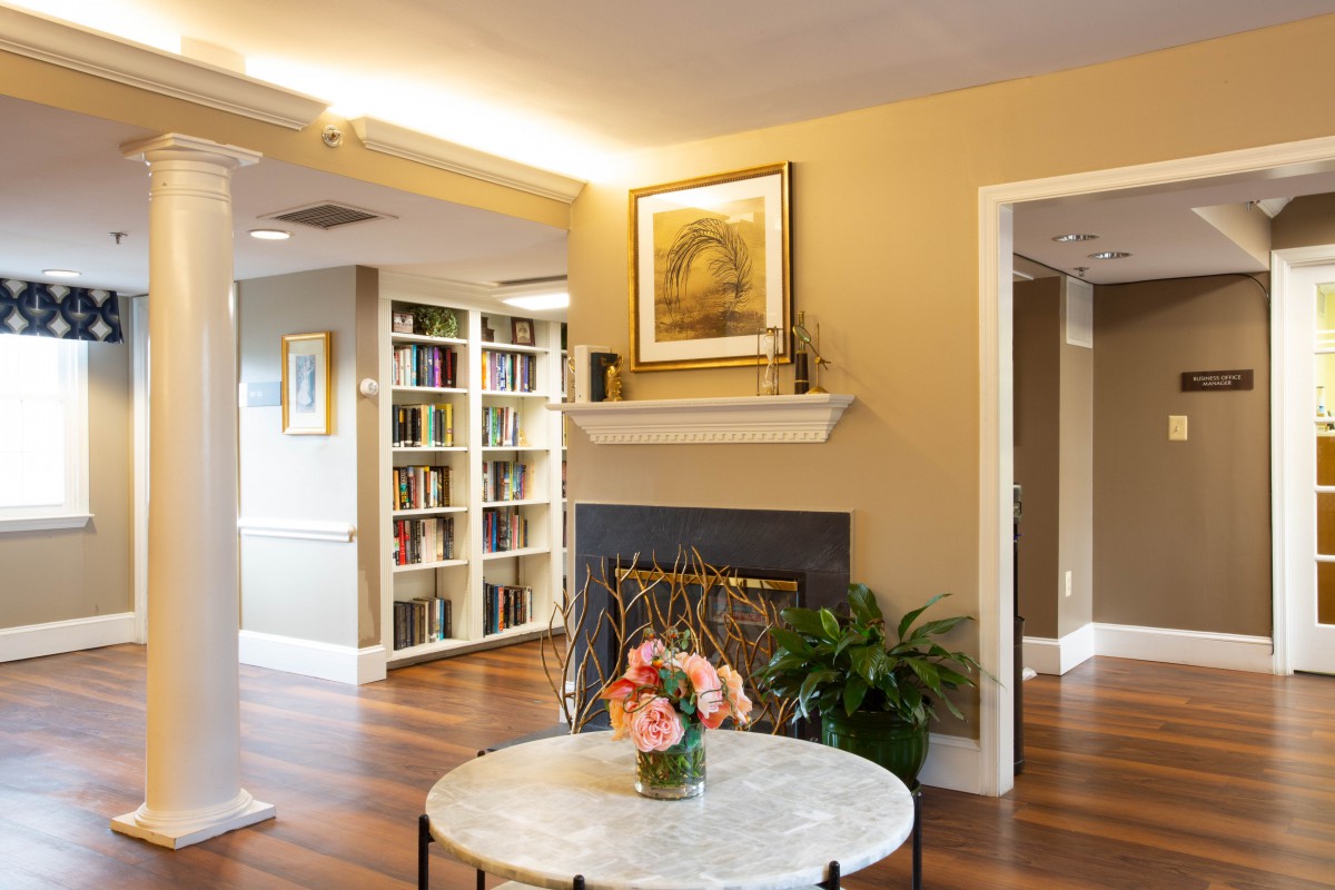 A cozy living room with a fireplace, bookshelves, and a round table adorned with flowers.
