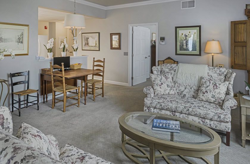 A cozy living and dining area with floral patterned sofas, a wooden dining table, and framed artwork on the walls.