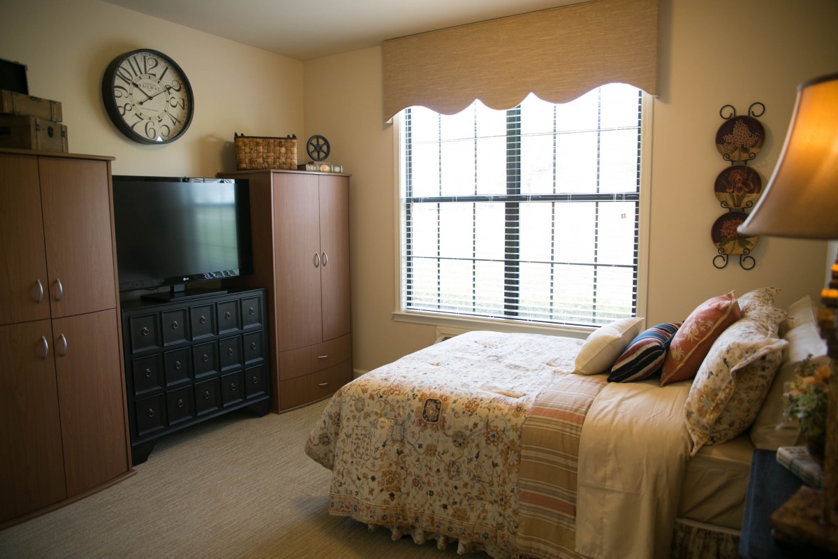 A cozy bedroom featuring a bed, television, and a large window with natural light.
