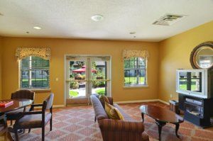 A cozy living room with a sofa, chairs, and coffee table, featuring large windows and a glass door opening to a garden.