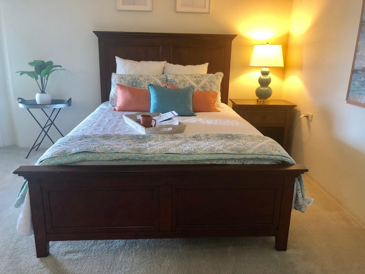 A cozy bedroom with a neatly made bed, colorful pillows, and a warm lamp on the nightstand.