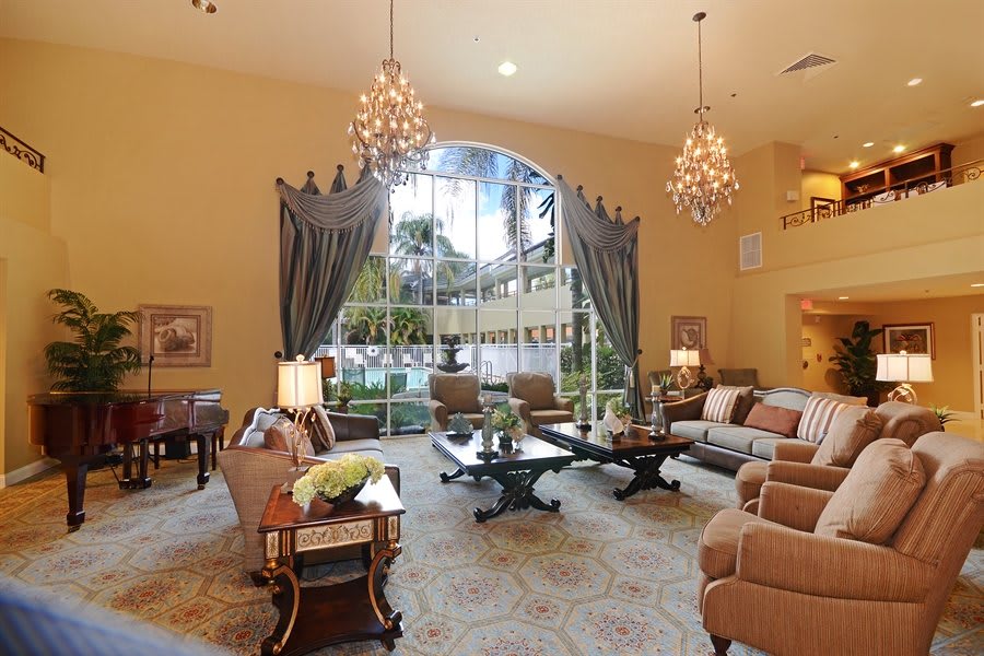 A luxurious living room with elegant chandeliers, plush furniture, and a large window with draped curtains.