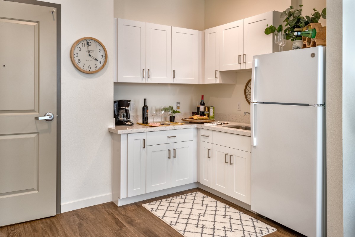 A modern kitchen with white cabinetry and appliances, featuring a coffee maker, wall clock, and decorative elements on the countertop.