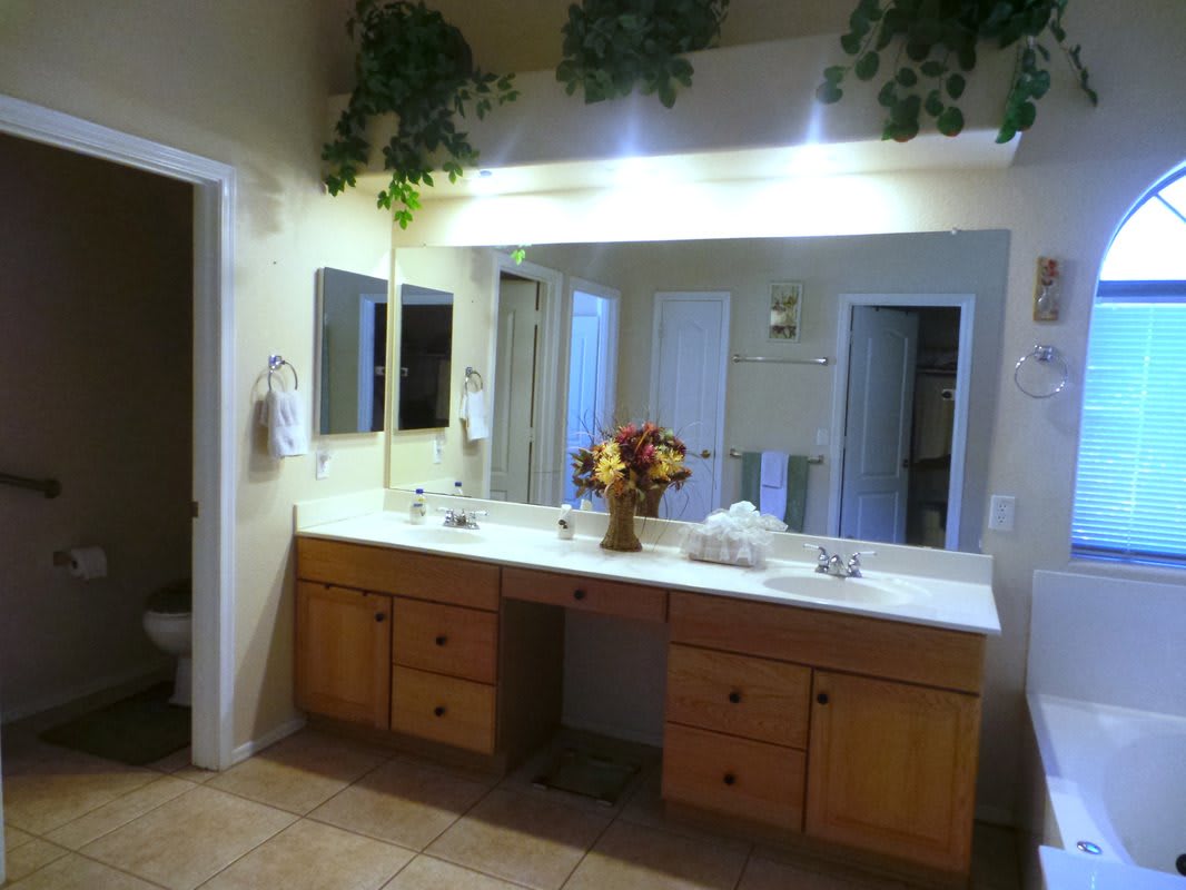 A well-lit bathroom with a large mirror, wooden vanity, and decorative flowers.