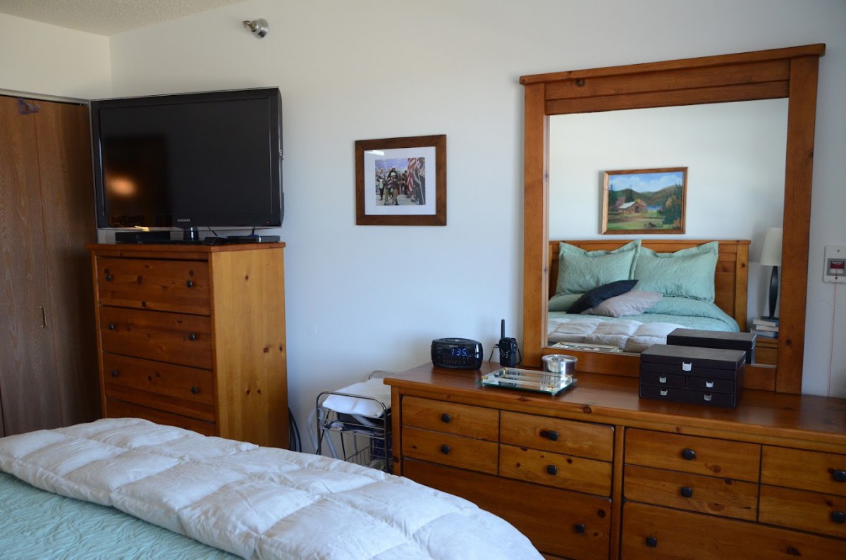 A cozy bedroom featuring a dresser with a mirror, a TV, and neatly made bed.