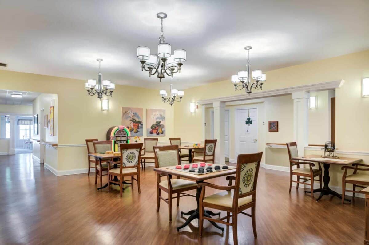 A well-lit dining area with multiple tables and chairs, featuring chandeliers and artwork on the walls.
