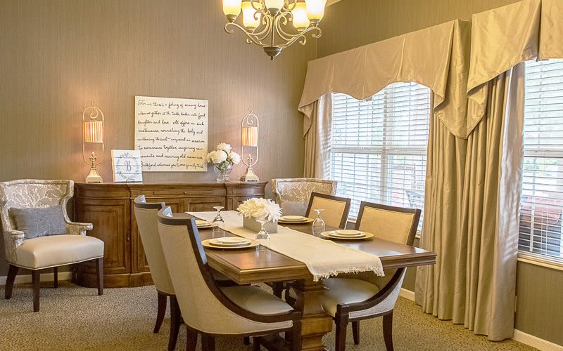 A warmly decorated dining room with a wooden table, cushioned chairs, and elegant lighting.
