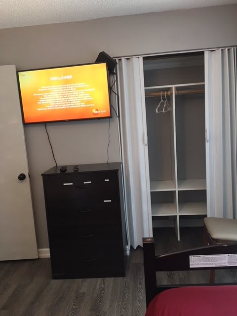 A bedroom setup with a mounted TV, dresser, and open closet.