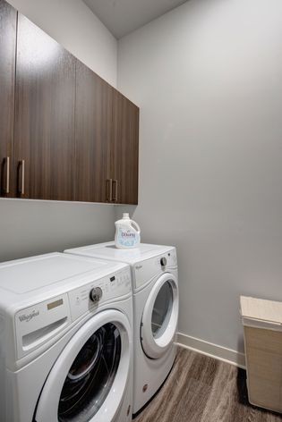 A modern laundry room with a washer and dryer set beneath wooden cabinets.