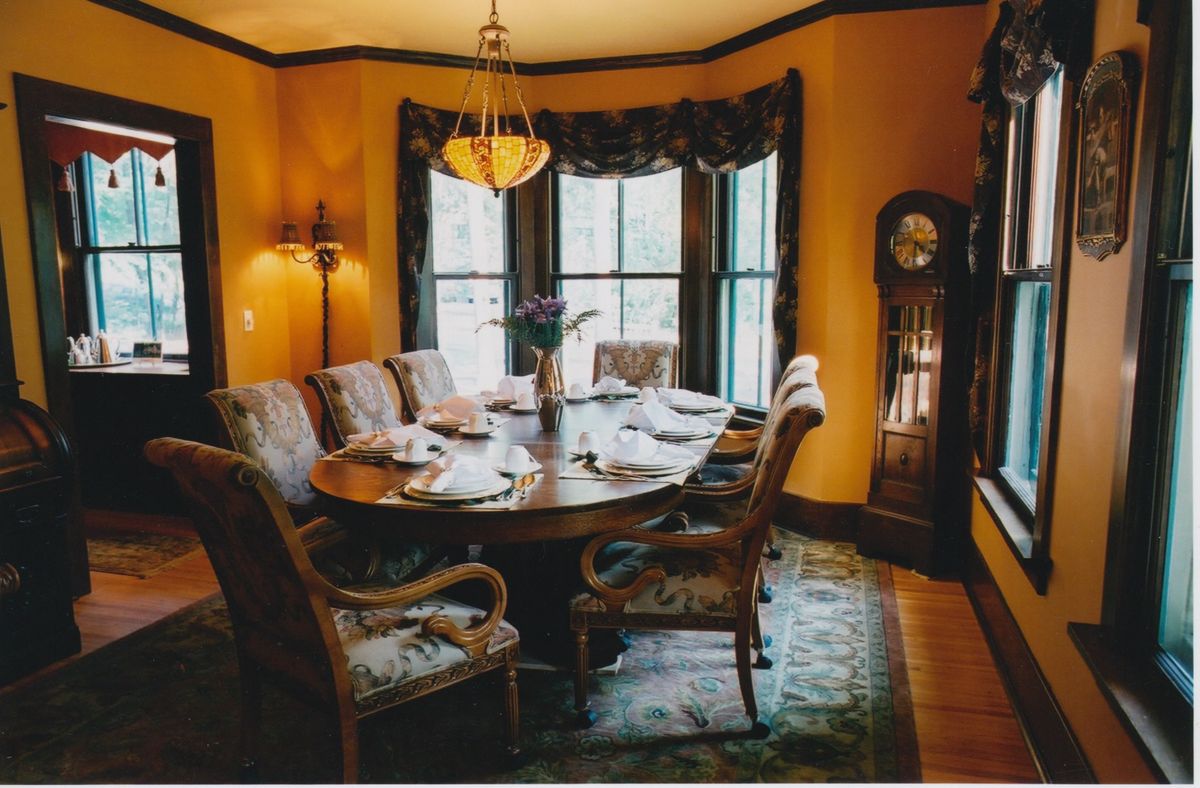 A beautifully decorated dining room featuring a classic wooden table, elegant chairs, a chandelier, and a grandfather clock.