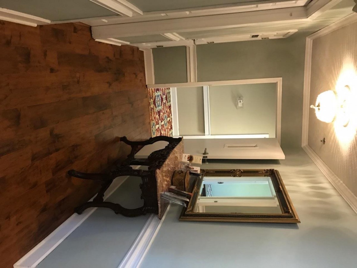 A cozy hallway featuring a wooden floor, an elegant chair, and a large framed mirror above a small table.