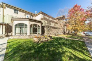 A sunny day view of a residential house with a spacious lawn and colorful autumn trees.