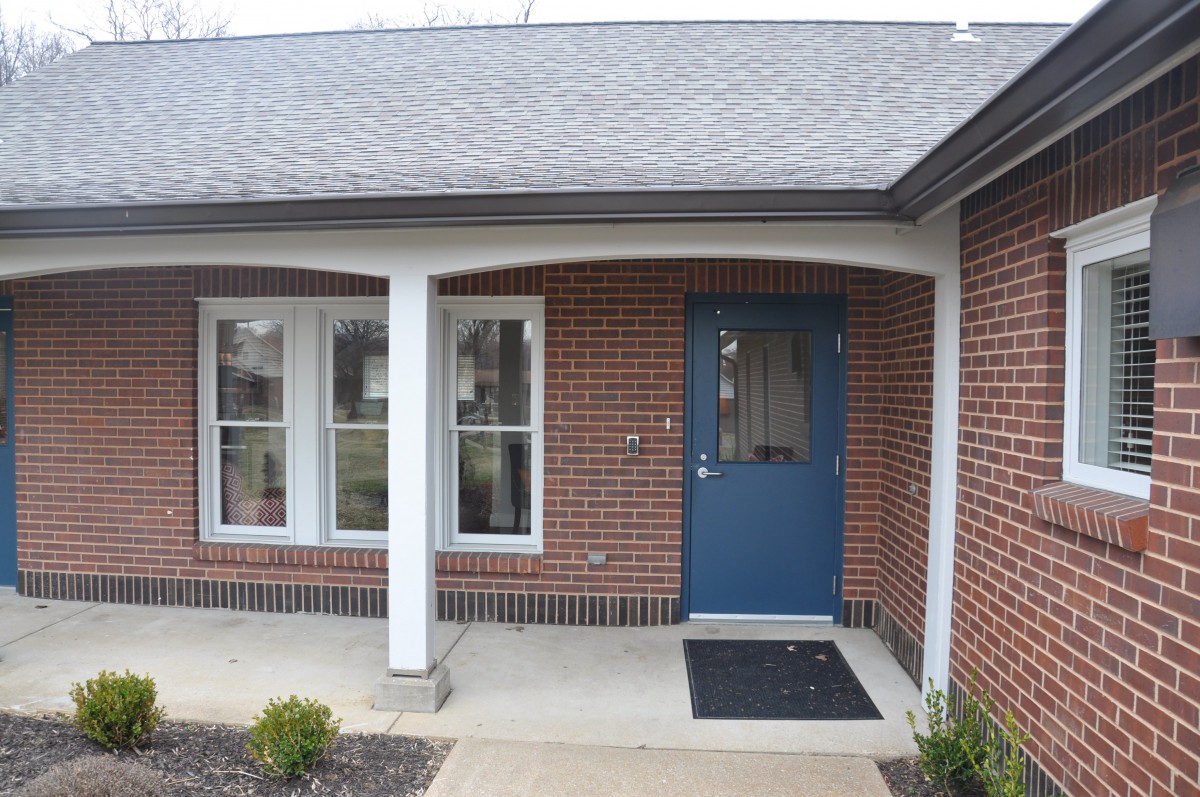 The front entrance of a brick house with a blue door, windows, and columns.