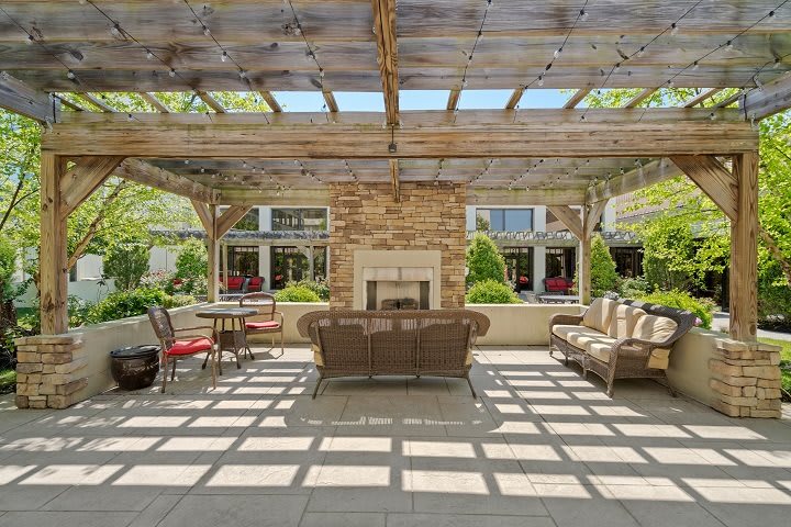 A cozy outdoor patio with a pergola and a central fireplace surrounded by comfortable seating.