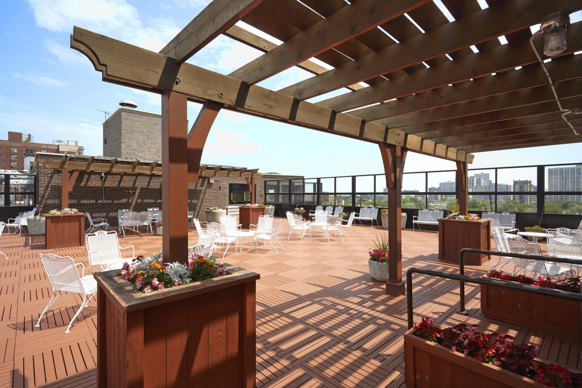A spacious city rooftop terrace with a pergola and outdoor seating on a sunny day.