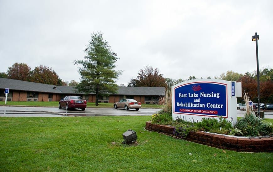 Entrance of East Lake Nursing and Rehabilitation Center with visible sign and parked cars.