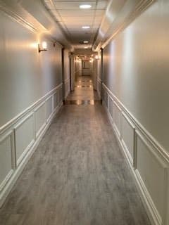 A long, well-lit hallway with elegant wall paneling and wooden flooring.