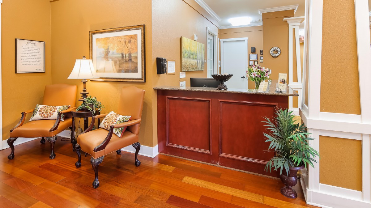 A cozy reception area with wood flooring, warm-colored walls, and elegant furnishings, including a desk and comfortable seating.