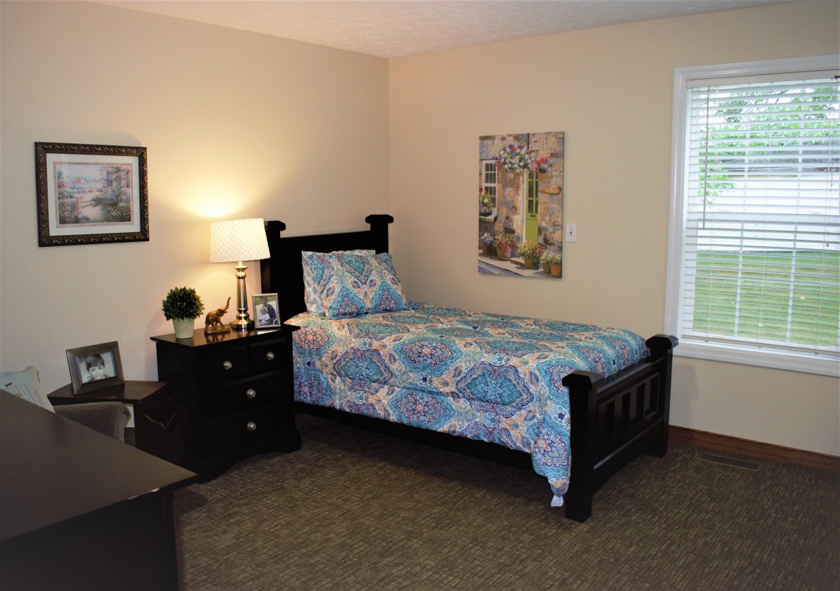 A cozy bedroom featuring a single bed with patterned bedding, a nightstand with a lamp, and decorative artwork on the wall.
