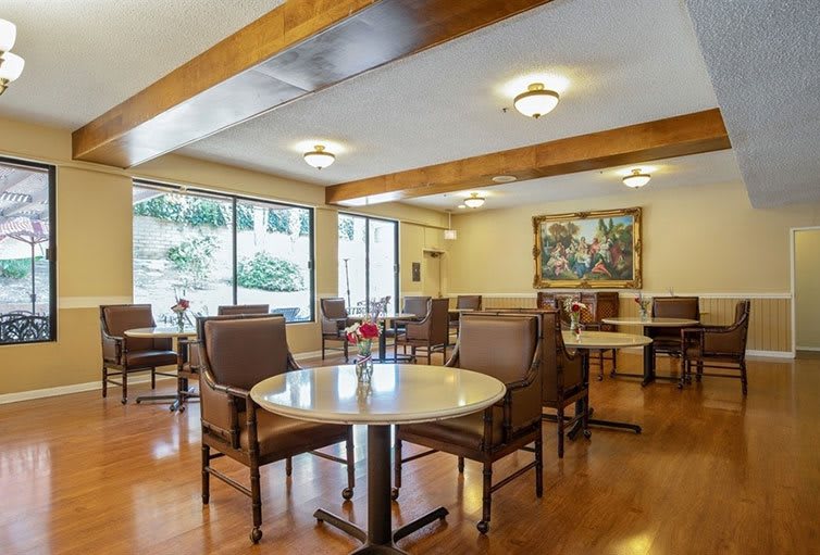 A cozy dining area with several tables and chairs, featuring a wooden floor and artwork on the wall.