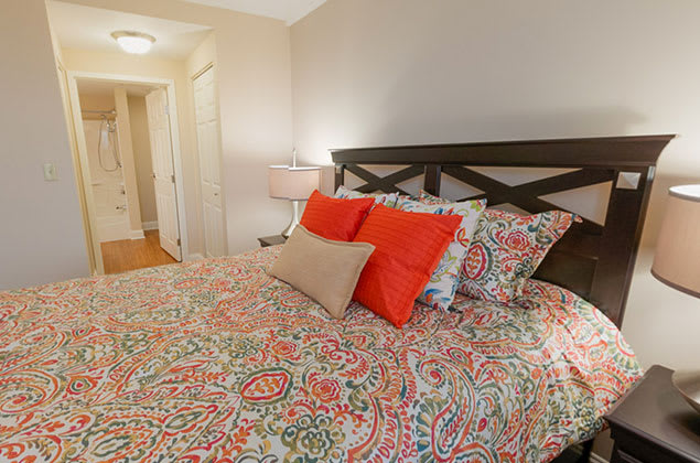 A cozy bedroom featuring a bed with colorful bedding and accent pillows, complemented by a bedside lamp.