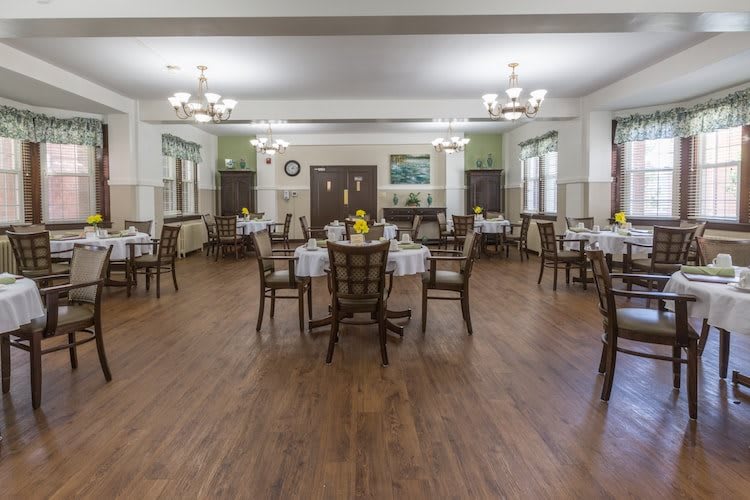 An empty dining room with neatly arranged tables and chairs, featuring a wooden floor and elegant chandeliers.