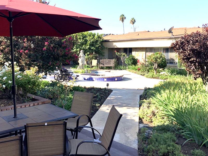 A tranquil garden patio with outdoor furniture and a red umbrella on a sunny day.