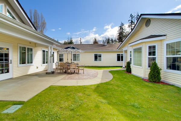 A serene backyard with a well-maintained lawn and patio furniture, surrounded by residential buildings under a clear blue sky.
