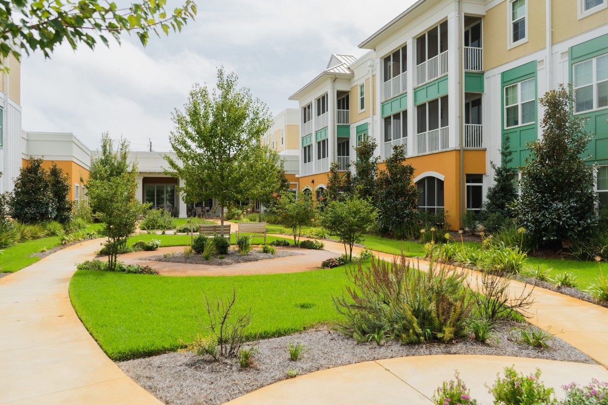 A modern building surrounded by a well-maintained garden with lush greenery and paved pathways under a cloudy sky.