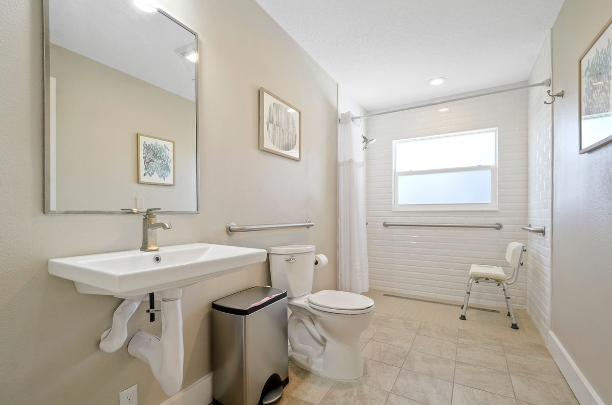 A spacious and accessible bathroom with a large mirror, sink, toilet, and window.