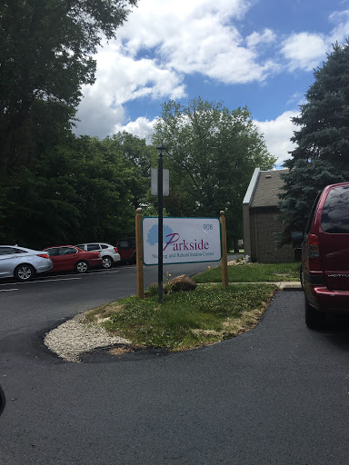Entrance to a facility with a parking area surrounded by trees under a partly cloudy sky.