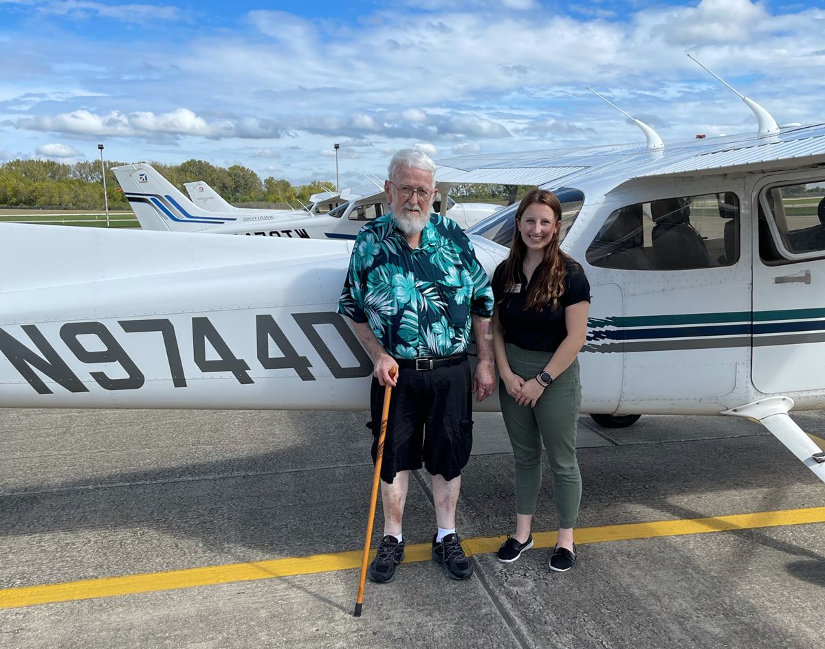 Two people standing in front of a small airplane on a tarmac.