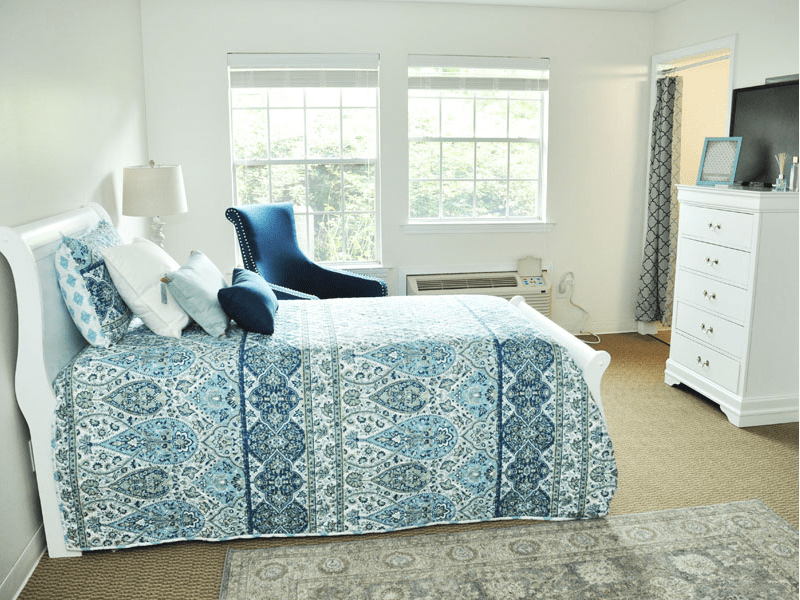 A bright bedroom with patterned bedding and a comfortable chair by the window.