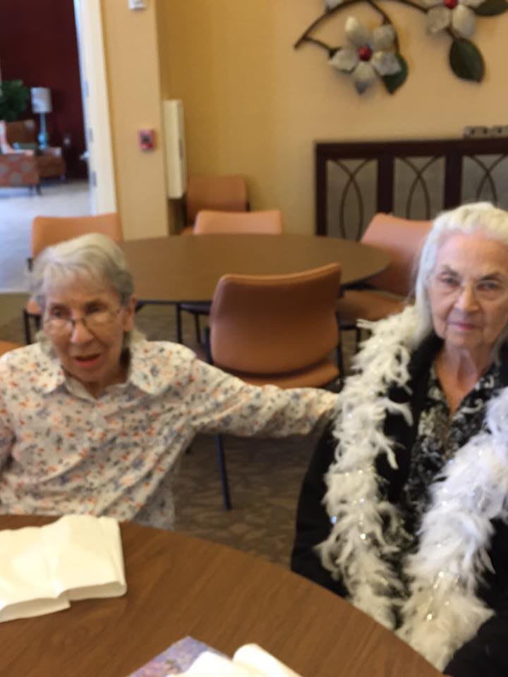 Two elderly women sitting together at a table in a communal setting.