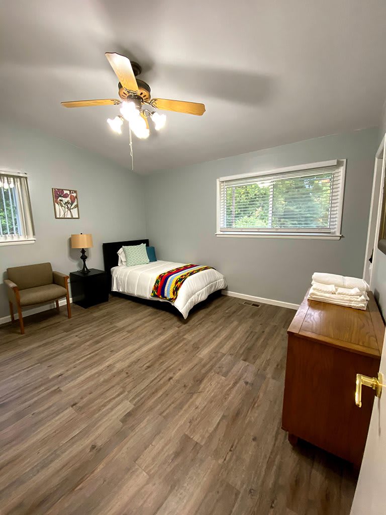 A spacious bedroom with a single bed, wooden flooring, and a ceiling fan.
