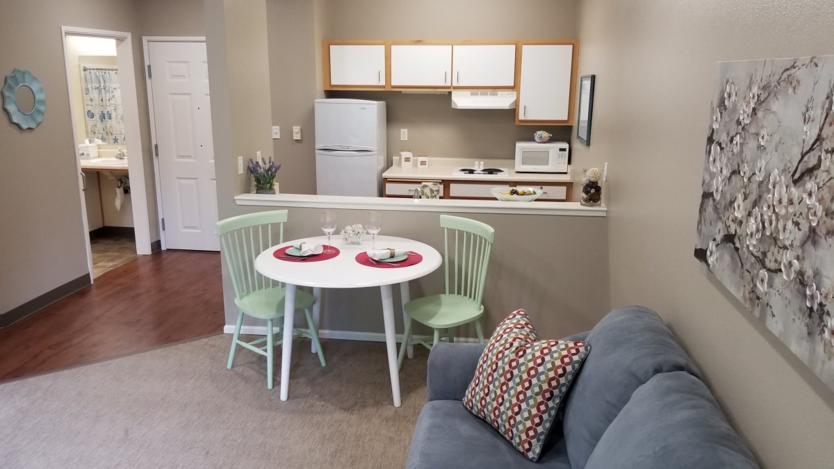 A small apartment kitchen with a dining area, featuring a table set for two, a compact refrigerator, and essential cooking appliances.