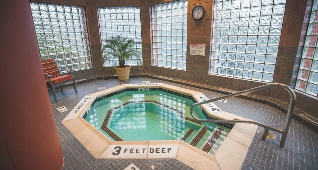 An inviting indoor hot tub with a depth of 3 feet, surrounded by glass block walls and plant decor.