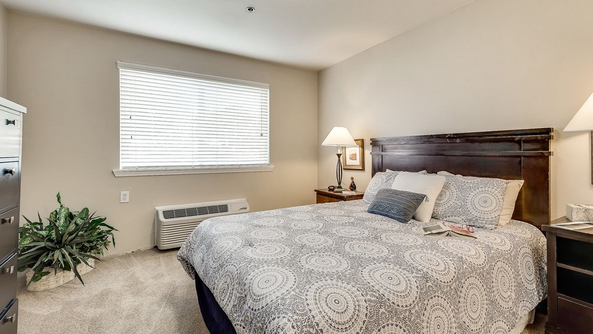 A cozy bedroom with a neatly made bed and a lamp on a bedside table.
