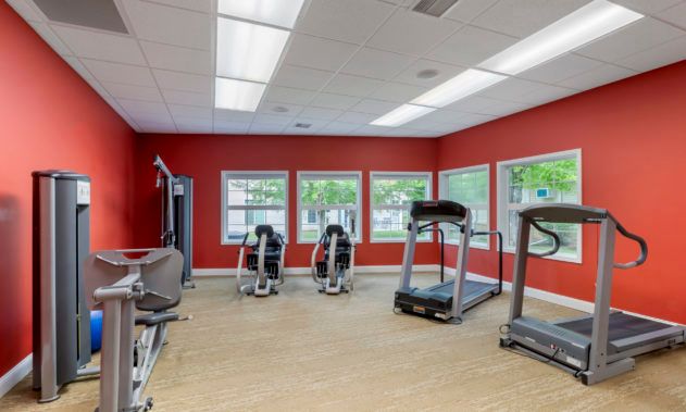 A bright gym room with treadmills and exercise equipment against red walls.