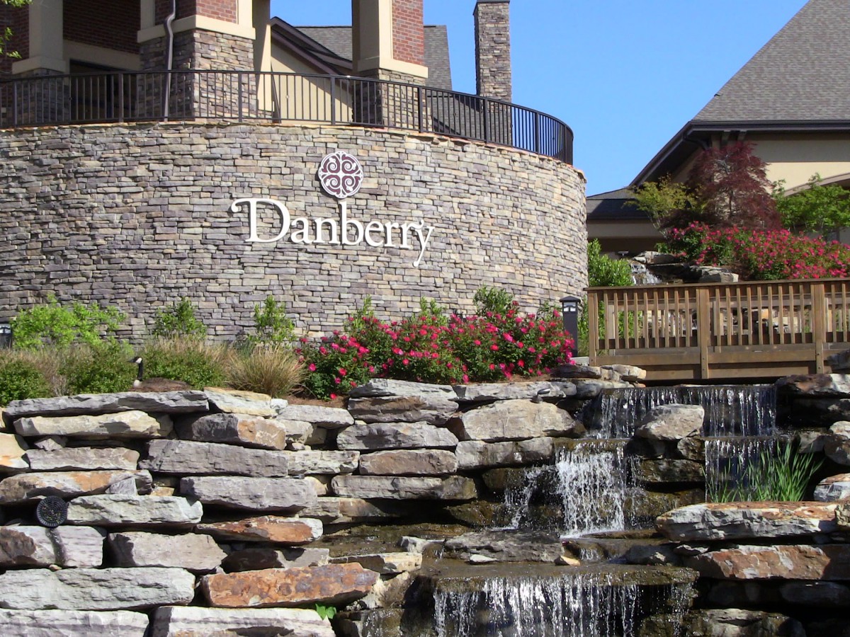 A scenic view of a stone waterfall overlooking the entrance sign 'Danbury' at a residential complex.