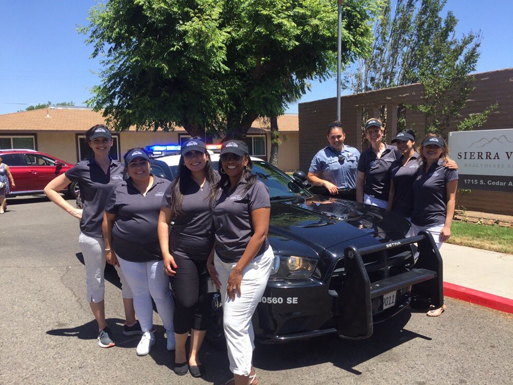 A group of people standing beside a police car on a sunny day.