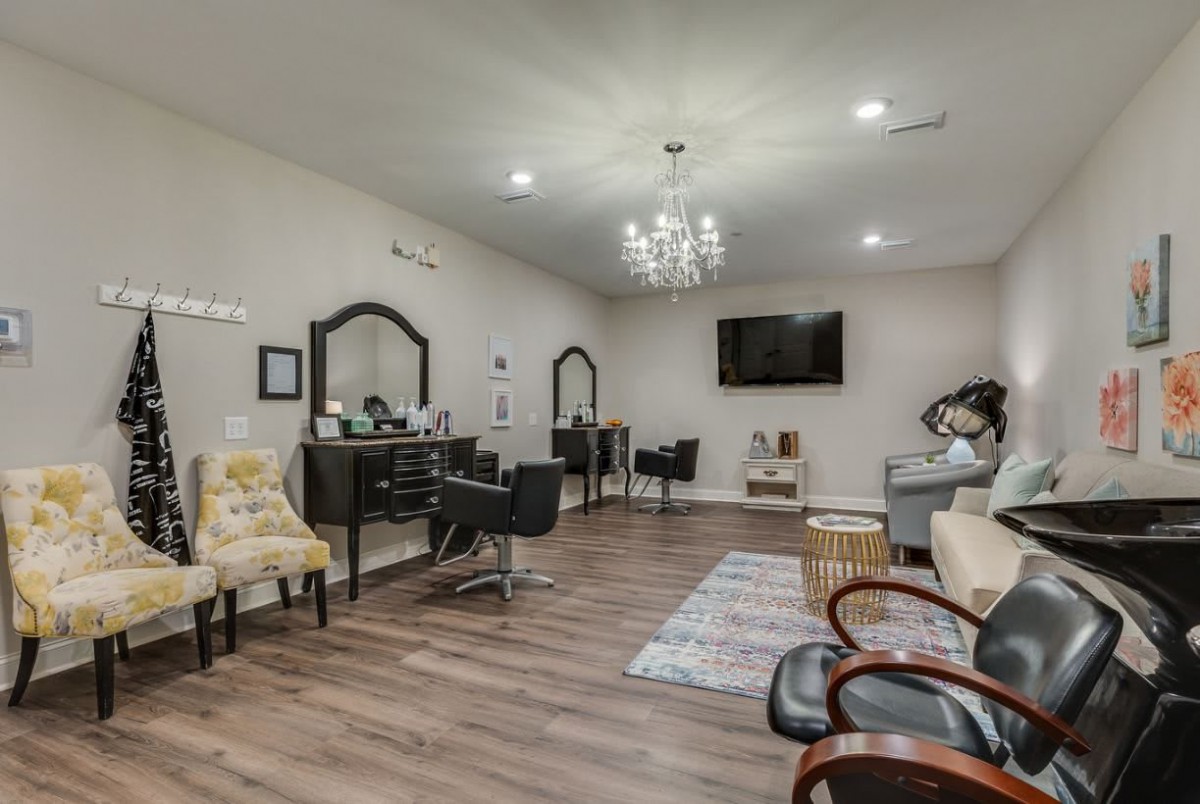 A modern salon interior featuring stylish chairs and mirrors, with a chandelier and wooden flooring.