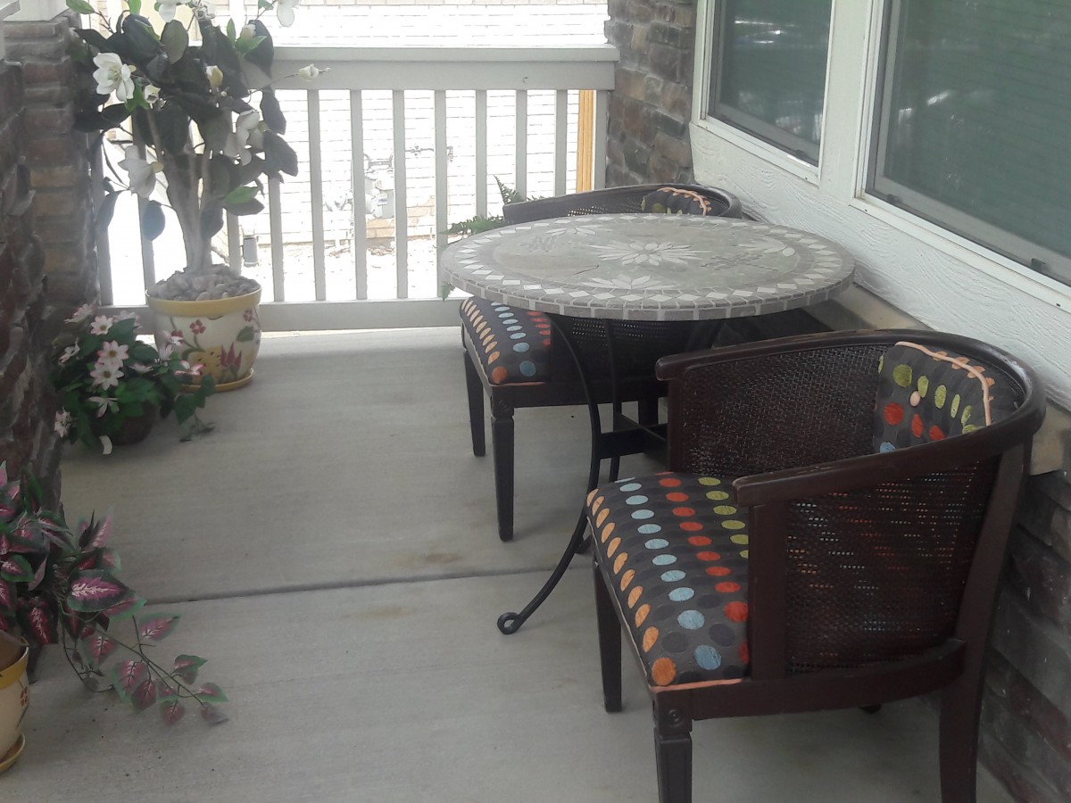 A cozy outdoor patio area with a table, two chairs, and a potted plant.