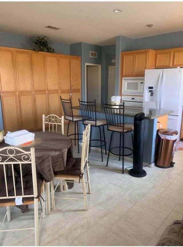 A cozy kitchen and dining area featuring wooden cabinets, a refrigerator, a table with chairs, and bar stools.