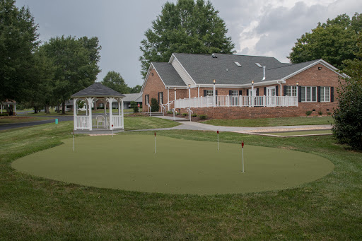 A serene backyard featuring a well-maintained putting green and a gazebo, surrounded by lush greenery.