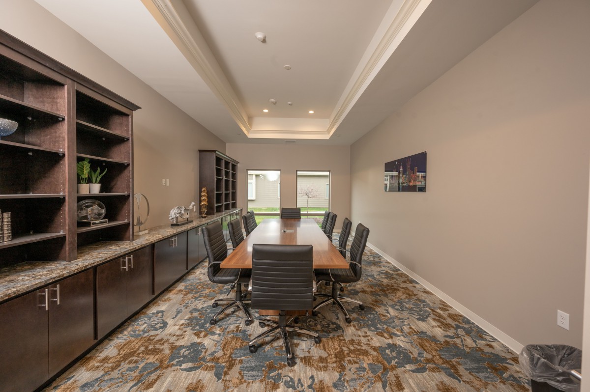 A modern conference room with a large table and chairs, featuring stylish lighting and carpet.