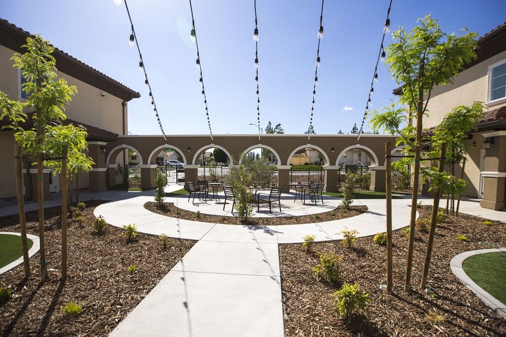 A beautifully designed outdoor courtyard featuring string lights and archways with a central seating area surrounded by landscaping.